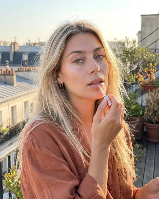 A beauty creator putting on lip gloss on a balcony