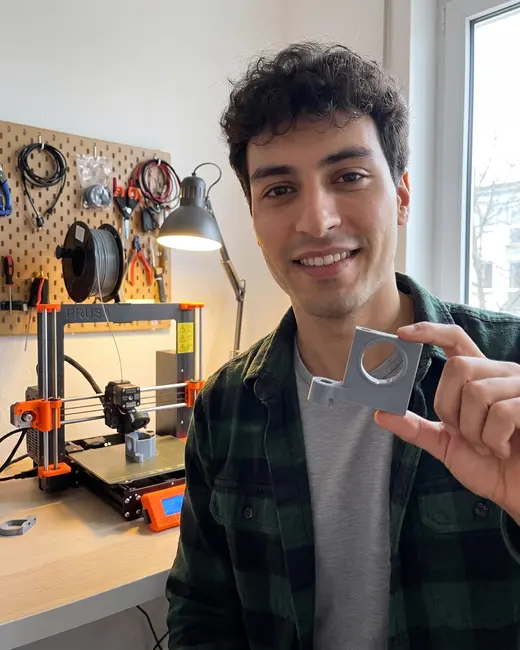 A tech creator showing a 3D-printed part in his workshop